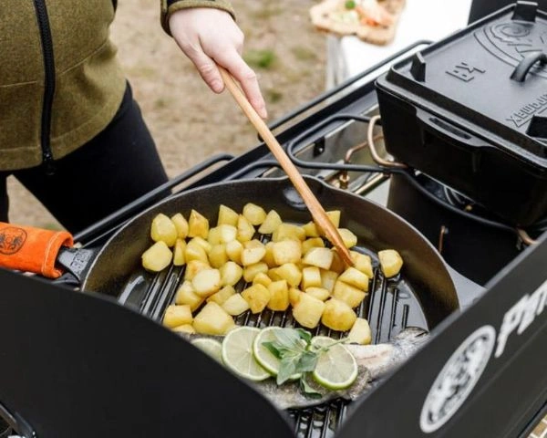 Persoana care gateste bucati de cartofi si peste in tigaie grill din fonta pe gratar